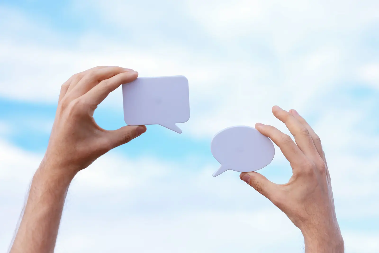 Two hands holding up speech bubbles against a blue sky