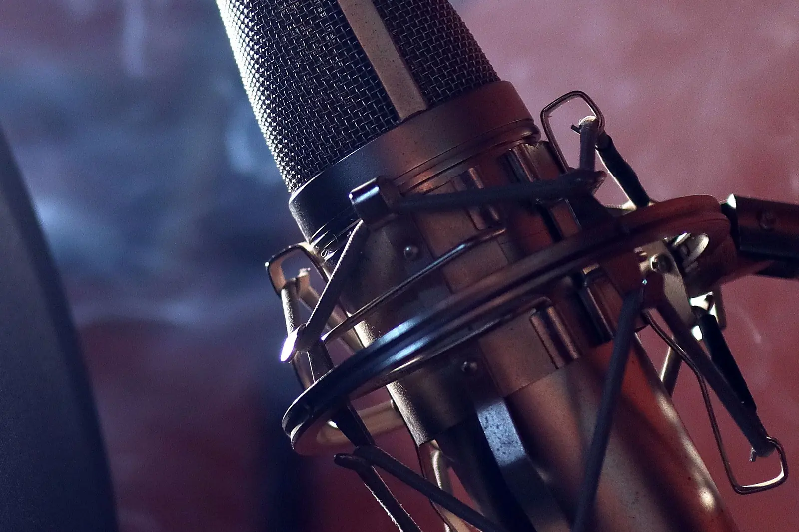 A studio microphone in its shock mount, lit purple through haze