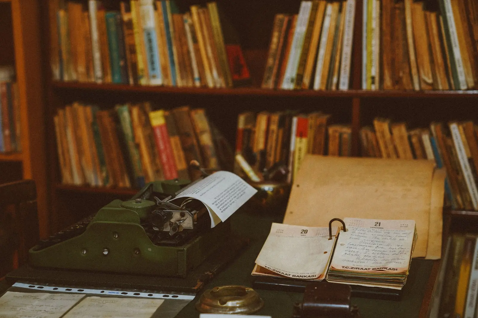 A typewriter and a handwritten diary in front of shelves of old books