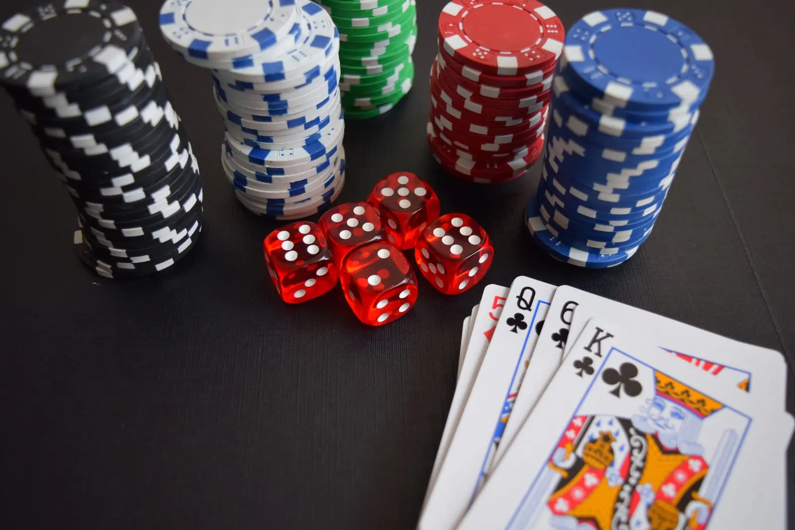 Stacks of poker chips, red dice and playing cards on a dark table