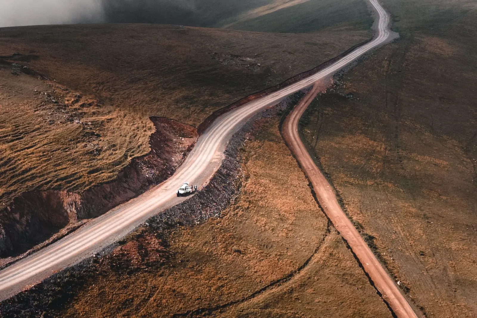 A car on a long road winding across open hills, seen from above